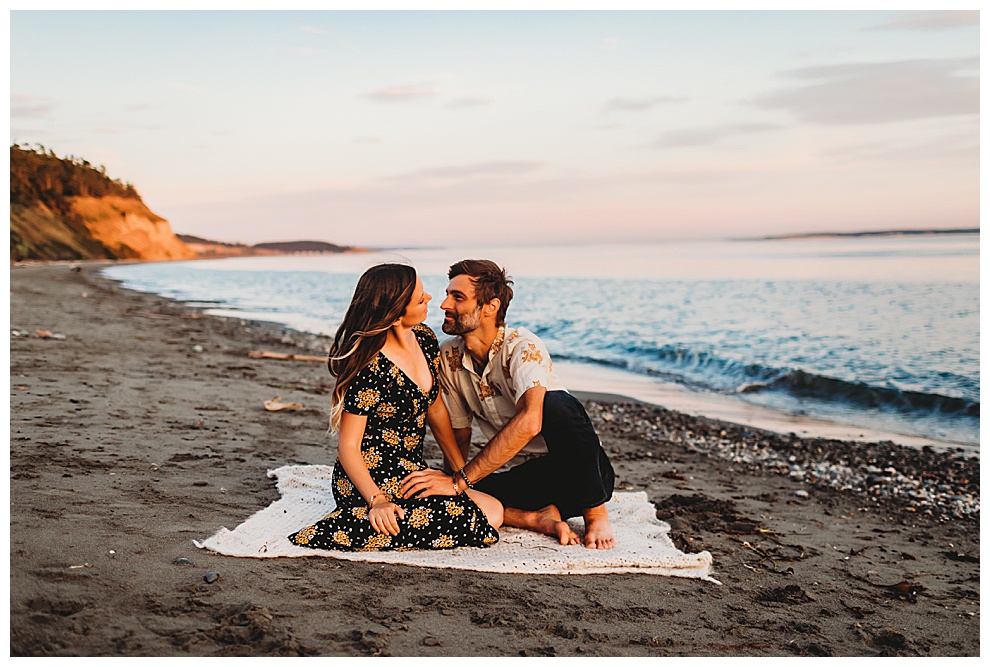couple sitting on picnic blanket on beach at sunset