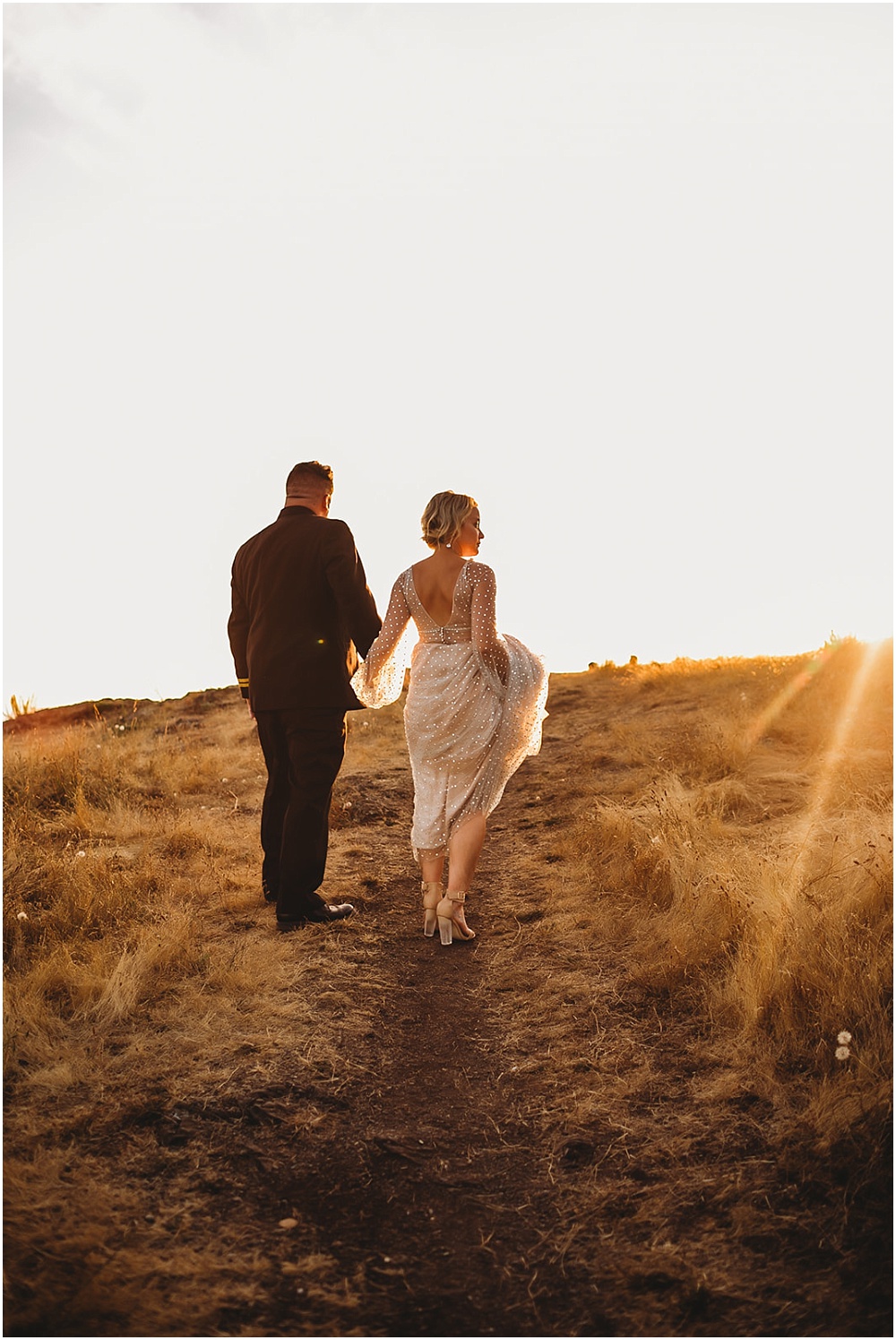 Bride and groom walking in field at sunset